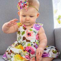 Eloisa Dresses in one of Karousel Kids Handmade Cotton Floral Baby Dresses with a bright Bow headband.